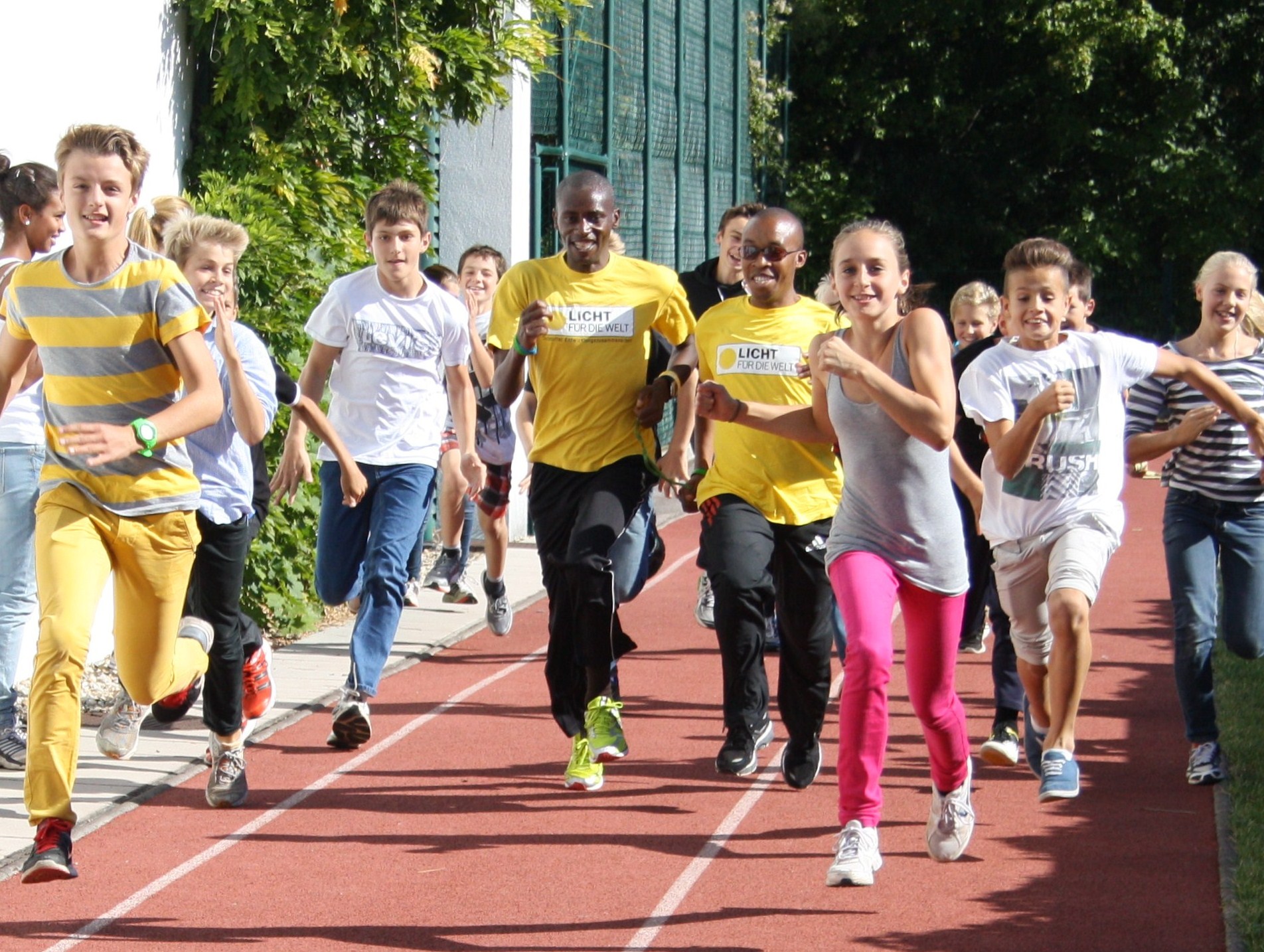 Kinder und zwei afrikanische Läufer gemeinsam auf einer Rennbahn
